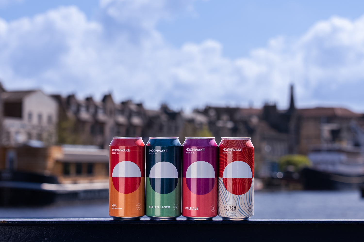 Four moonwake beer cans with a blurred cityscape in the background
